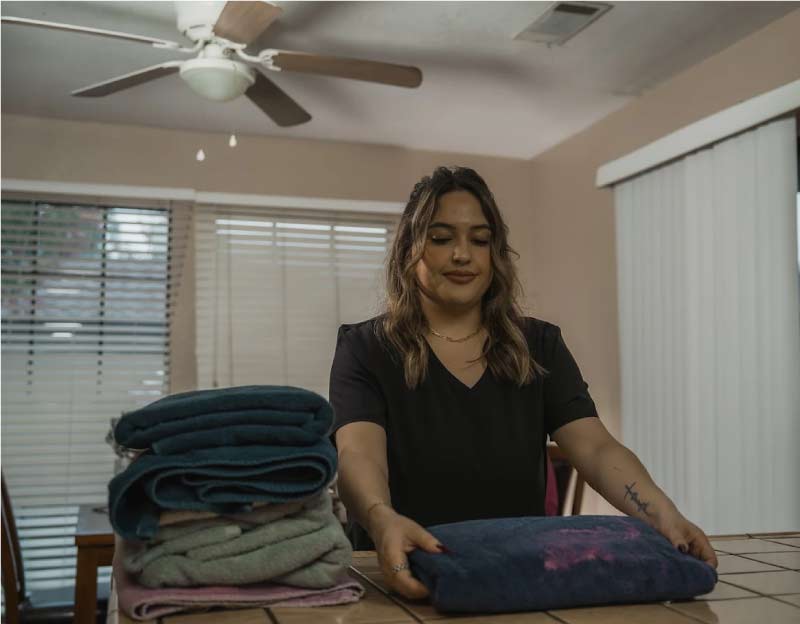 A dedicated home care attendant neatly folding fresh laundry and towels as part of light housekeeping services for a senior client